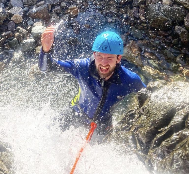 man cheering whilst climbing to the top of a waterfall at Stickle Ghyll