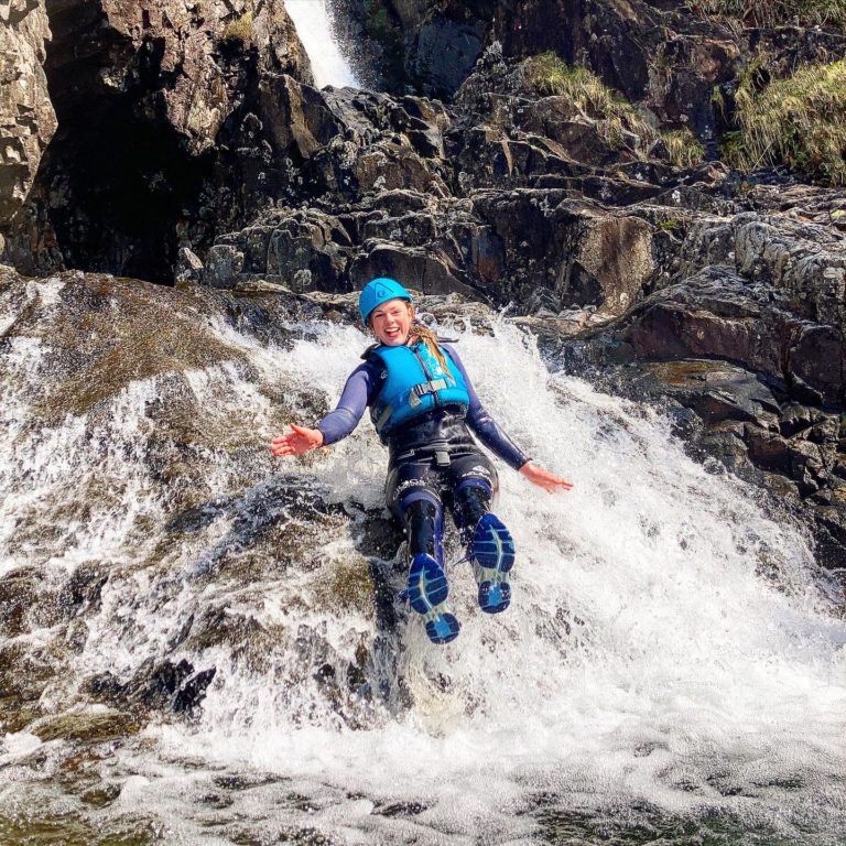 A woman laughing whilst sliding down a rock slide in the Lake District