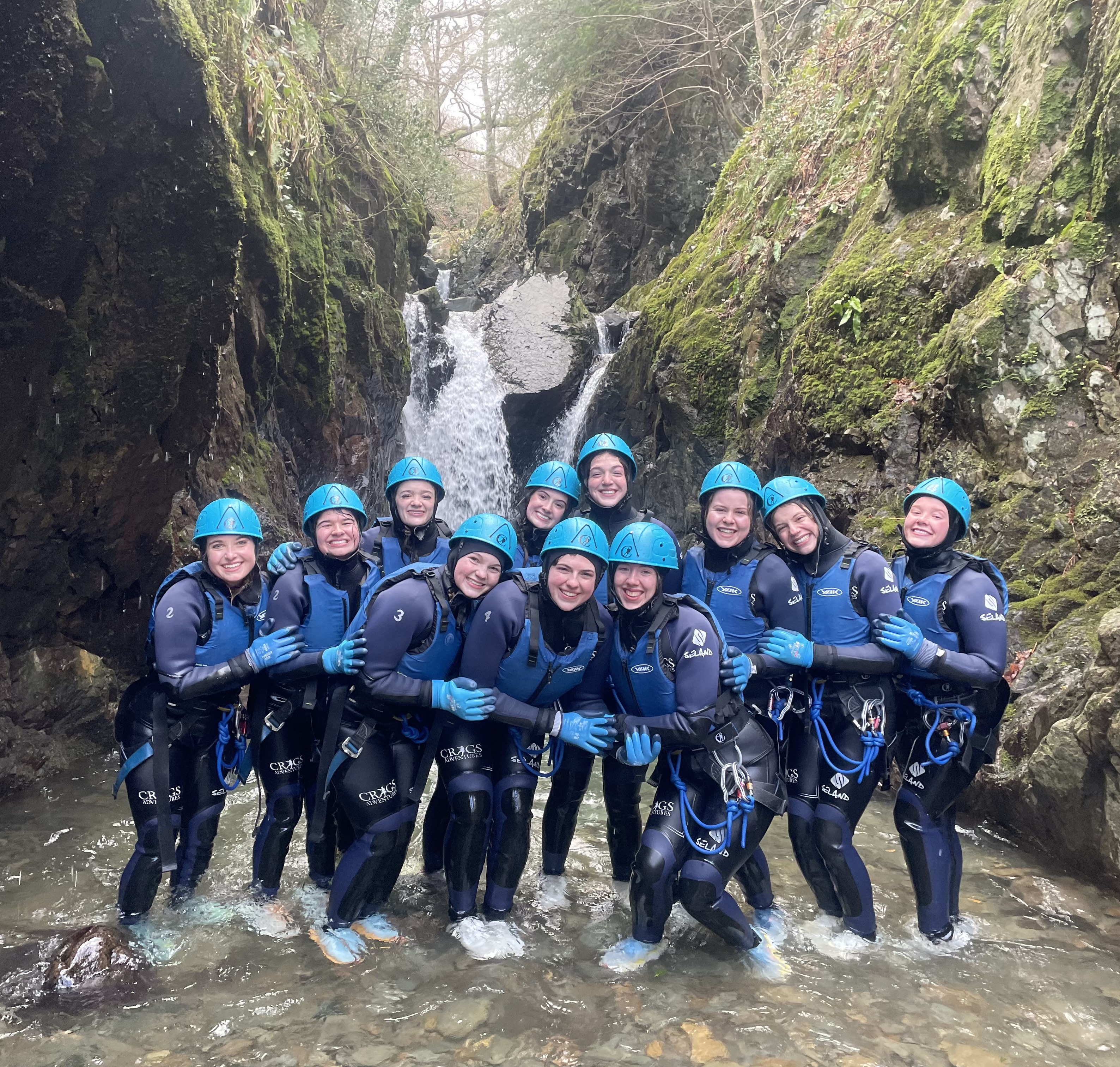 a group with full Winter canyoning gear on laughing in a mountain stream