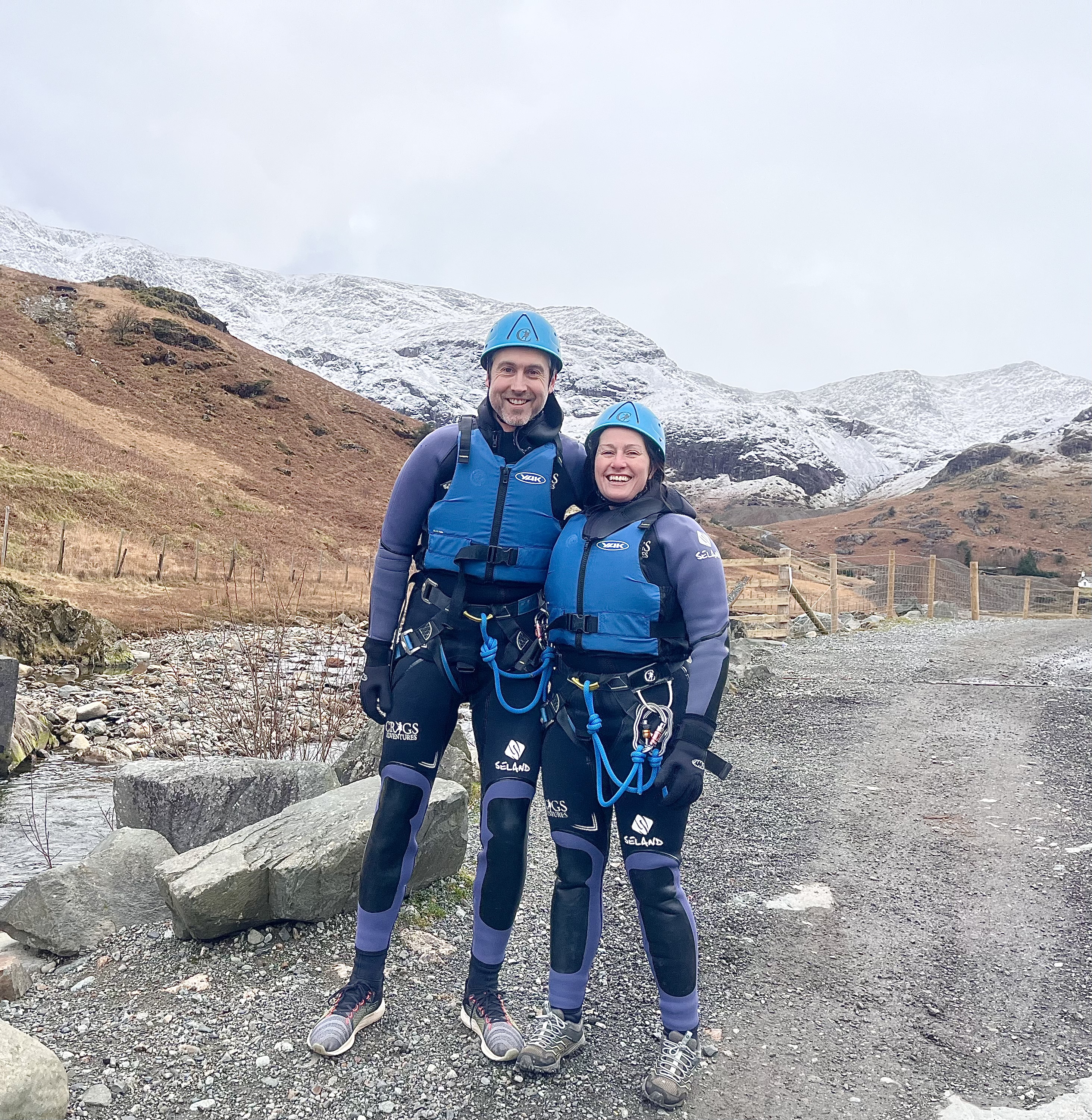 a couple dressed ready to start canyoning in the Winter with snowy scenes in the background