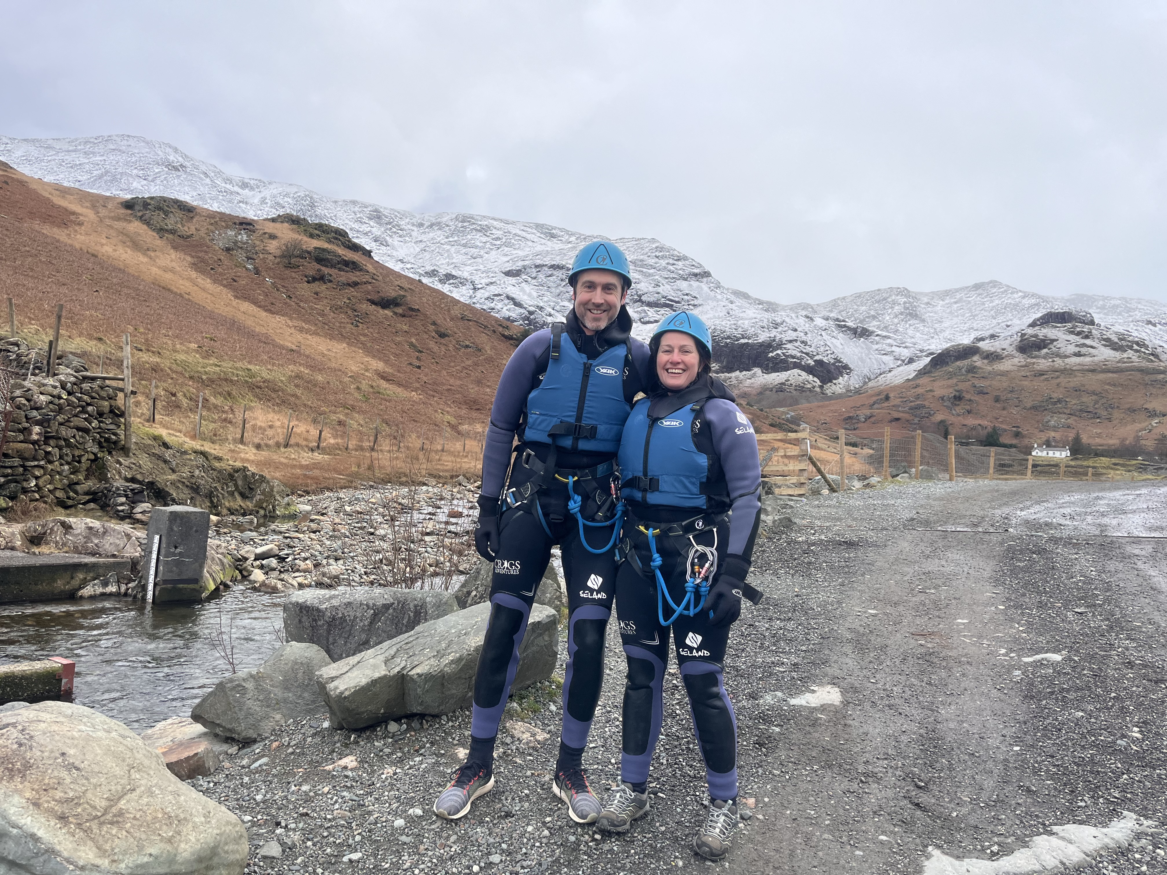 a couple stood with Coniston fells behind them, ready to do a canyoning trip in canyoning equipment