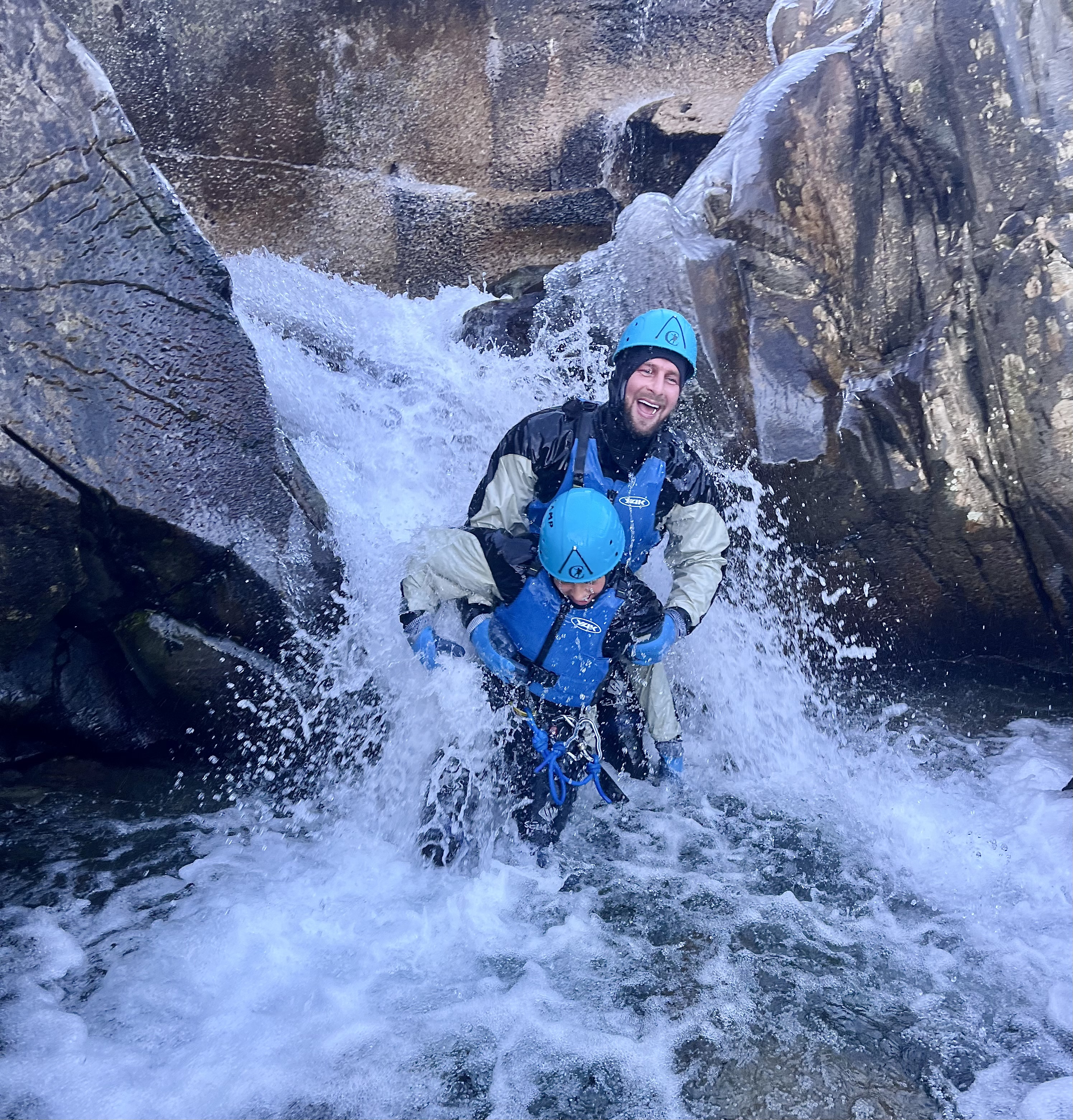 Dad and Son under a small waterfall during a canyoning trip