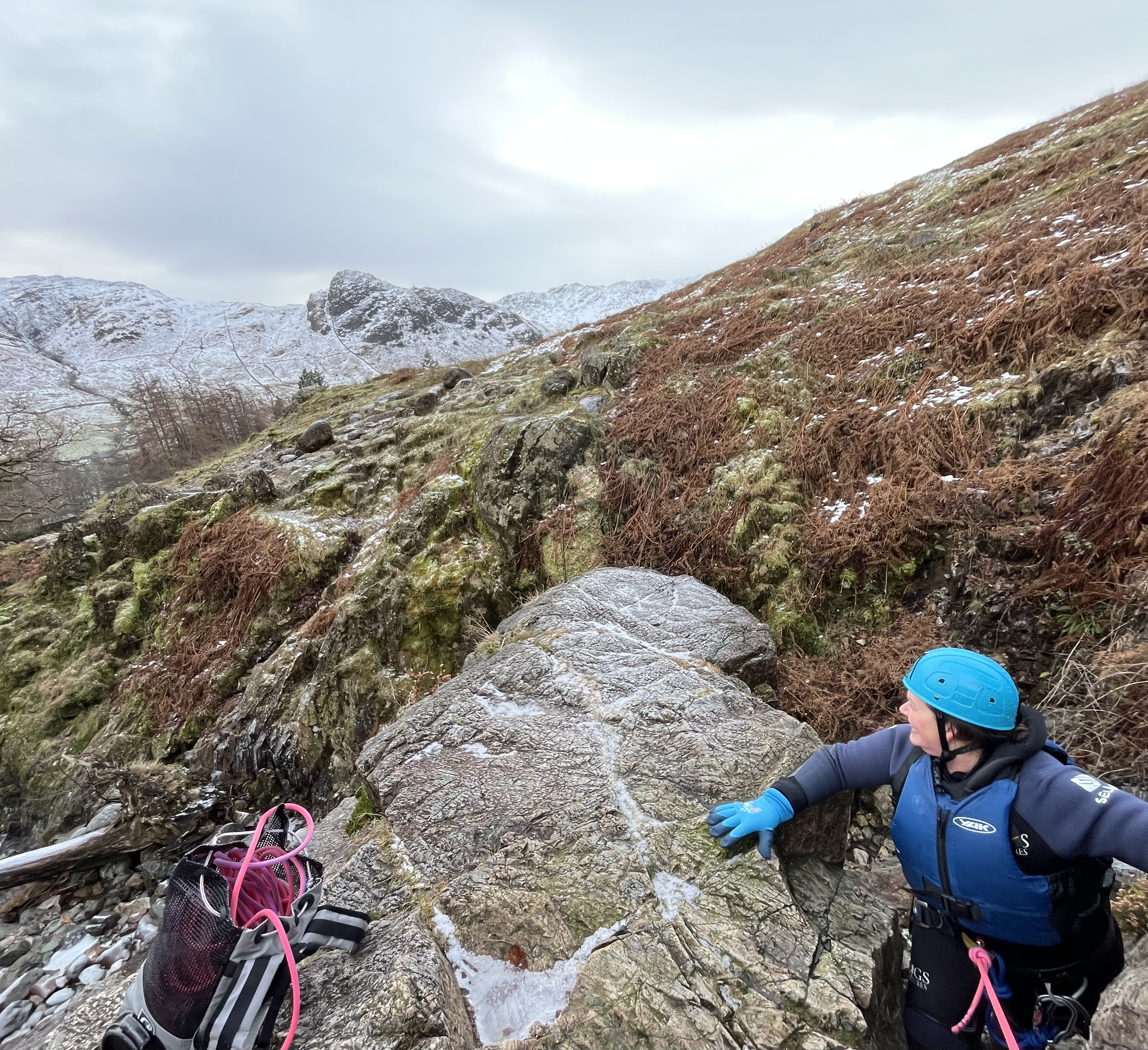 a person dressed in full Winter canyoning kit looks out towards the snow topped fells in the distance, in the Lake District