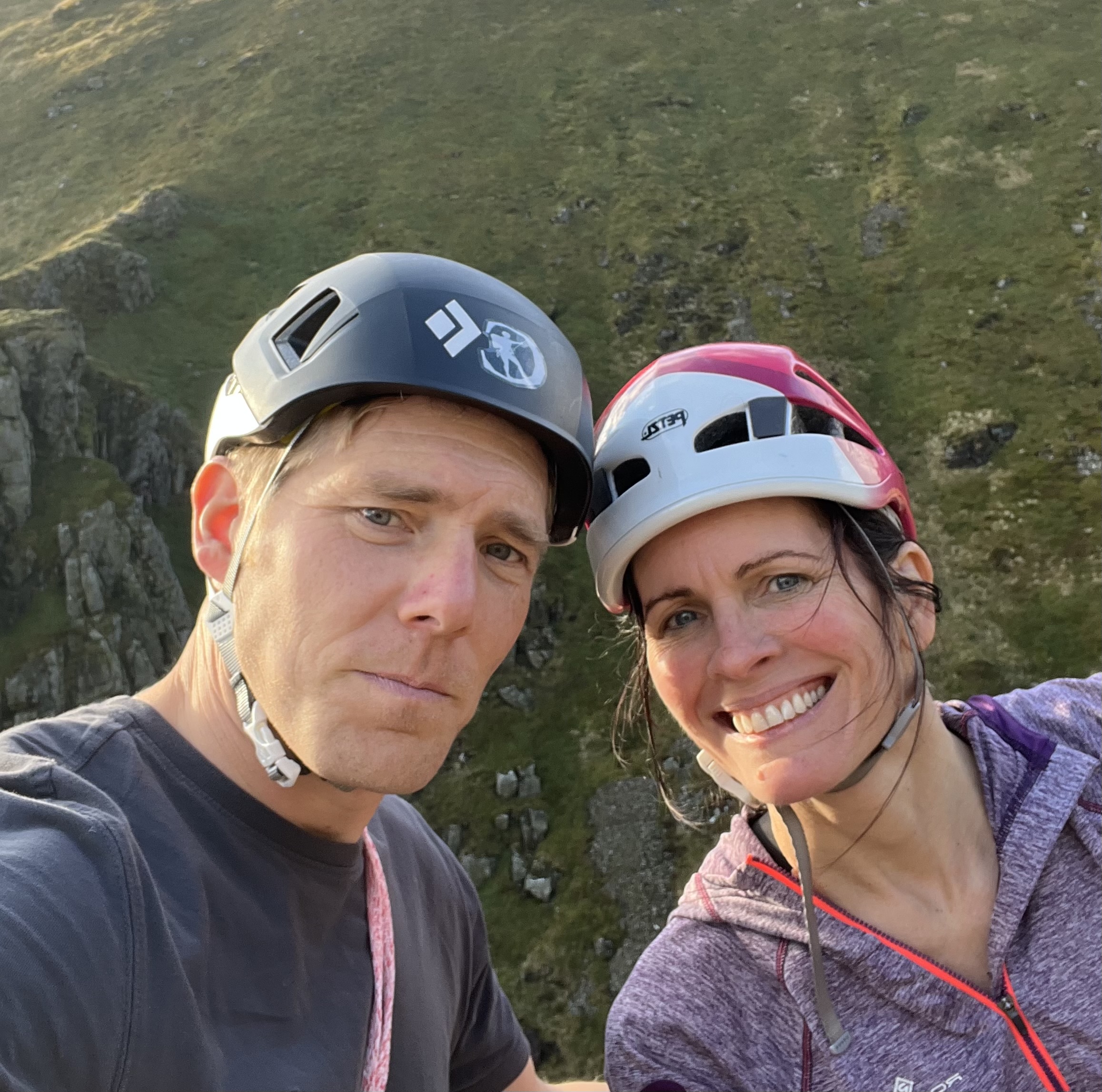 a man and woman wearing climbing helmets having a selfie in a mountain scene