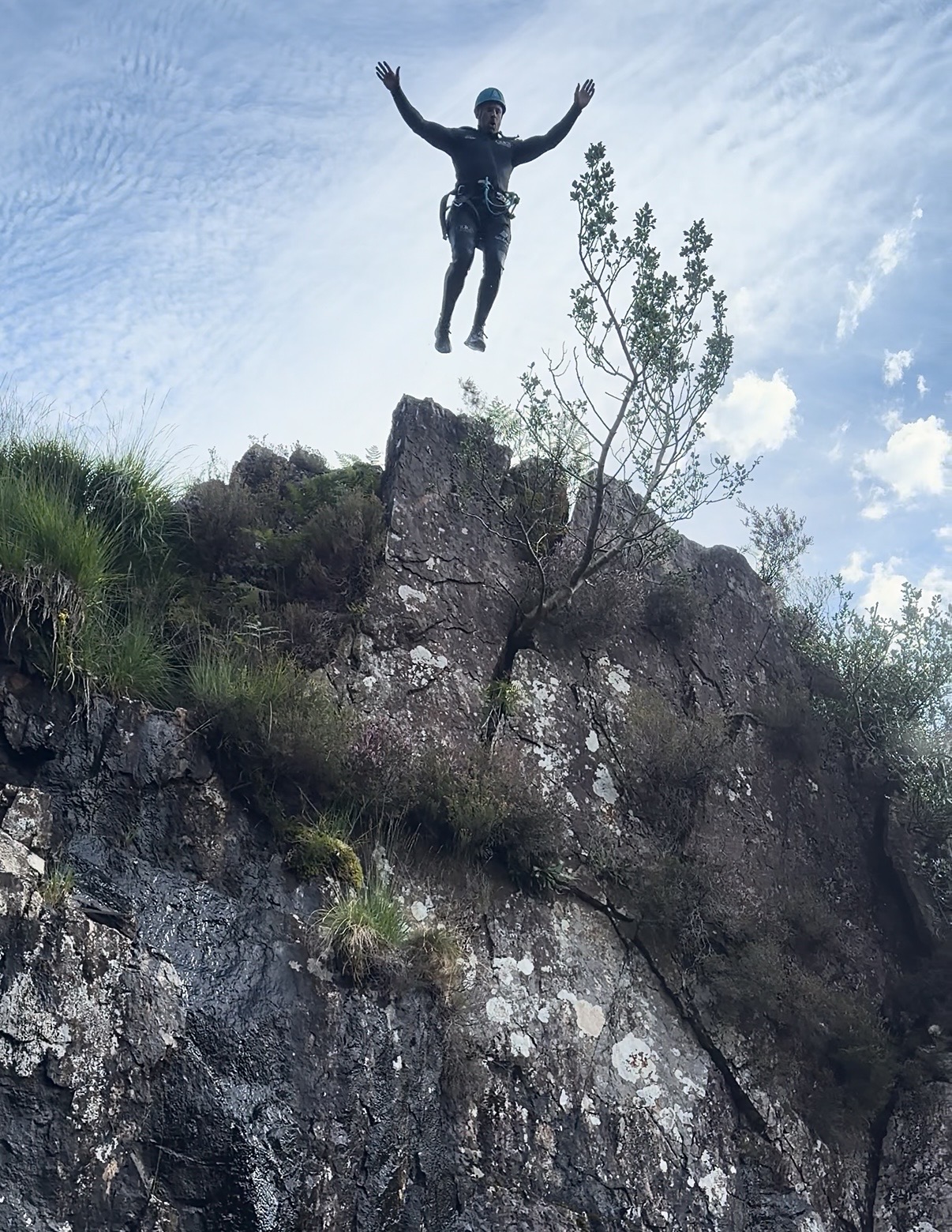 the silhouette of a person jumping off a cliff, with blue sky around them and rocky cliff below