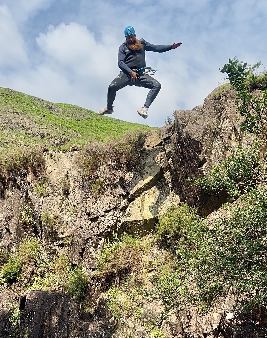 a man mid flight as he jumps off a cliff during an organised ghyll scramble in the Lake District