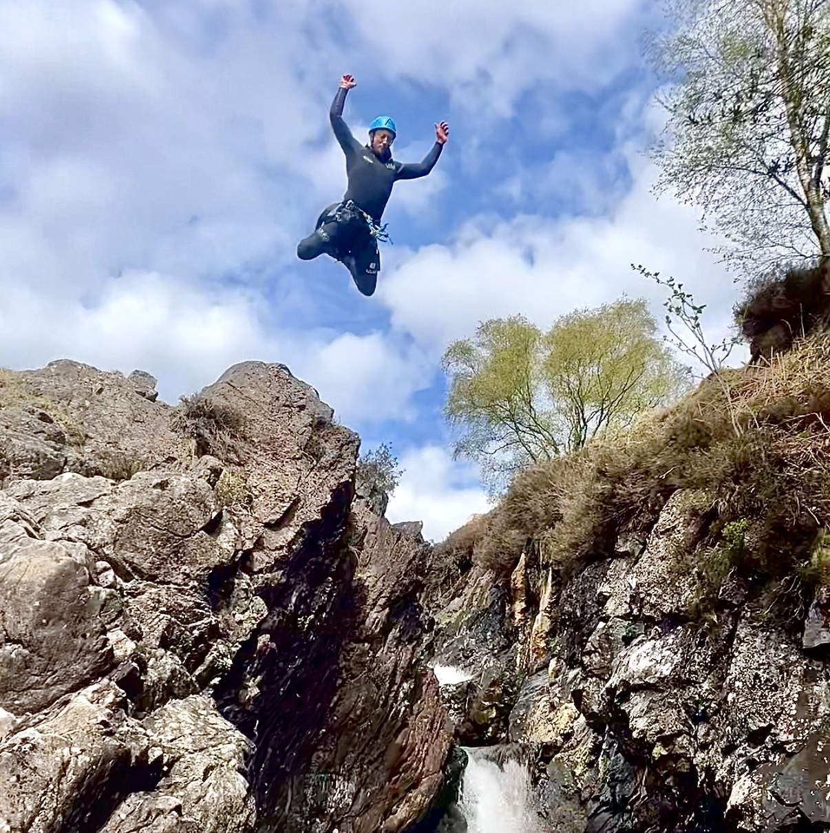a man that's jumping off a rocky cliff, with his arms in the air and legs tucked behind him